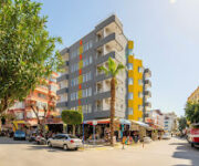 Kleopatra Icaria Apart Hotel’in modern binası, açık yüzme havuzu ve çevresindeki palmiyelerle birlikte Alanya güneşi altında görüntülenmiş