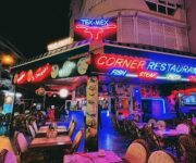 Corner Restaurant Alanya’da şık bir dış mekan masasında sunulmuş çeşitli deniz ürünleri, salatalar ve içecekler; arka planda Akdeniz manzarası ve yeşil bitkiler yer almakta.