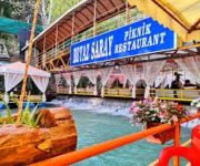 Alanya Dim Çayı restaurant da su üstü platformda serpme kahvaltı yapan insanlar, doğal manzara eşliğinde restoran keyfi.