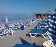 Blue Beach No:41 Alanya'nın turkuaz deniz manzaralı şezlongları, palmiye gölgeleri ve sahil kenarındaki modern beach bar alanı.