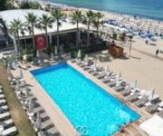 LOCO Beach Club Alanya’da palmiyelerle çevrili havuz başı alanı ve deniz manzaralı lüks şezlonglar