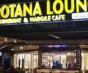 Mahmutlar’daki Rotana Loung’un otantik dekorlu iç mekanı, rahat oturma grupları ve küçük masalar; arka planda raflar üzerinde şarap ve içecek şişeleri, müşteriler sohbet ediyor. Alanya