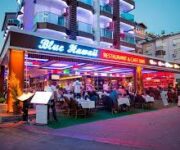 Kleopatra Blue Hawaii Restaurant’ta masalar, deniz manzarası eşliğinde şık bir akşam yemeği ortamı sunuyor.