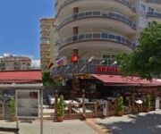 “Alanya sahilinde, palmiye ağaçları altındaki Pura Vida Restaurant’ın açık hava oturma alanı ve tropikal atmosferi.”