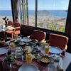 Kurşunlu Restaurant Alanya’da ağaçlarla çevrili, panoramik şehir ve deniz manzarasına sahip dış mekân; masalarda zengin mezeler, ızgara kebap tabakları ve içecekler sunulmaktadır.