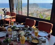 Kurşunlu Restaurant Alanya’da ağaçlarla çevrili, panoramik şehir ve deniz manzarasına sahip dış mekân; masalarda zengin mezeler, ızgara kebap tabakları ve içecekler sunulmaktadır.