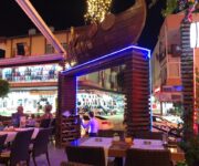 Melani Restaurant Alanya’da kaya dekorlu açık alanda ızgara et, makarna tabakları, nargile ve akşam yemeği sofrası.