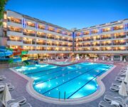 Avena Resort & Spa Hotel’in açık yüzme havuzu ve palmiyelerle çevrili tatil alanı, Alanya Oba’da yaz güneşi altında.