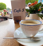 Cafe S’nin deniz manzaralı terasında renkli içecekler, kahve fincanları ve tatlı tabaklarıyla donatılmış bir masa gün batımında görüntülenmiş