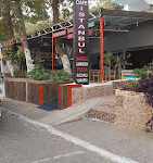 Cafe İstanbul Mek Pizza Tosmur’da servis edilen bol malzemeli, taş fırında pişmiş yuvarlak pizza; yanında ketçap, mayonez ve içecekle birlikte ahşap masada sunulmuş