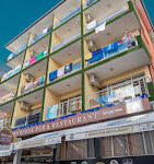 Kleopatra Bebek Otel’in giriş cephesi, balkonlu odaları ve palmiyelerle çevrili bahçesiyle birlikte gündüz ışığında görüntülenmiş