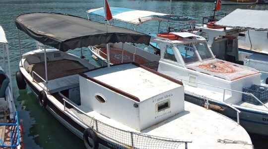 Alanya kıyısında demirli, 2006 yapımı sahibinden satılık ahşap gövdeli ve pancar motorlu özel tekne, güneşli bir günde görüntülenmiş.