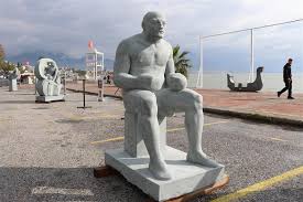 Taş heykel sempozyumunda bir sanatçının büyük boy mermer blok üzerinde çekiç ve oyma aletleriyle çalıştığı Alanya manzaralı sahne.