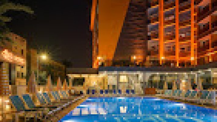 Arsi Hotel’in açık yüzme havuzu, palmiyeler ve modern otel binasıyla birlikte güneşli bir Alanya manzarasında görüntülenmiş