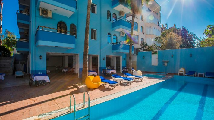 Barhan Hotel Alanya’nın açık yüzme havuzu ve balkonlu odalarla çevrili modern bina görünümü.