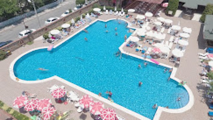 Club Sidar Apart Otel’in geniş açık yüzme havuzu, apart blokları ve şezlonglarla çevrili dinlenme alanı güneşli bir yaz gününde görüntülenmiş