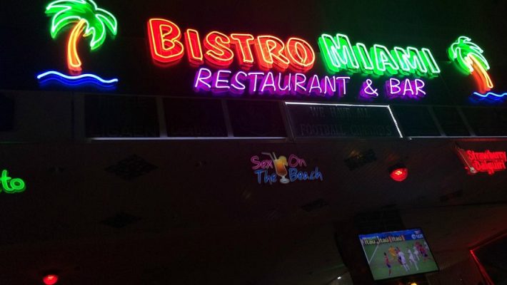 Bıstro Miami Restaurant & Bar Alanya’da şık dış mekân masasında kokteyller, mezeler ve Akdeniz esintili ana yemekler yer alıyor; arka planda palmiye ağaçları ve aydınlatılmış bahçe dekorları dikkat çekiyor.