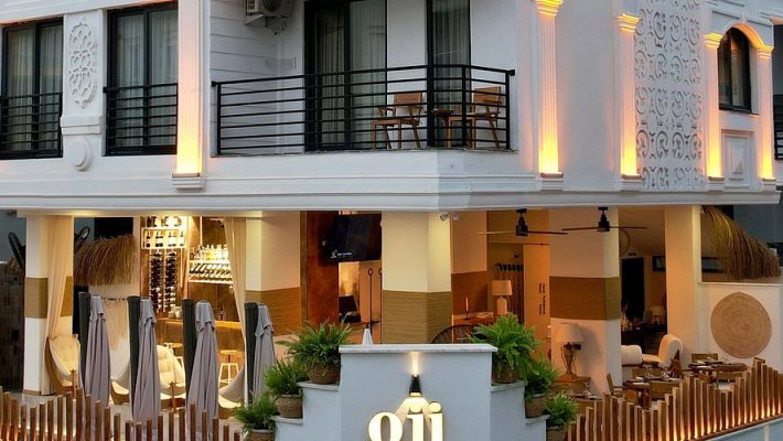 “Oji Resort Alanya’nın palmiyelerle çevrili büyük yüzme havuzu, havuz başı şezlong alanı ve modern otel binası.”