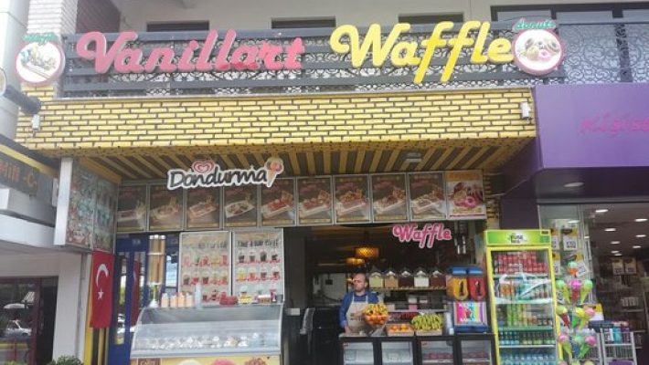 Alanya’da hizmet veren Vanillart Waffle & Cafe’nin dış cephesi ve renkli waffle sunumlarıyla süslenmiş masa görüntüsü