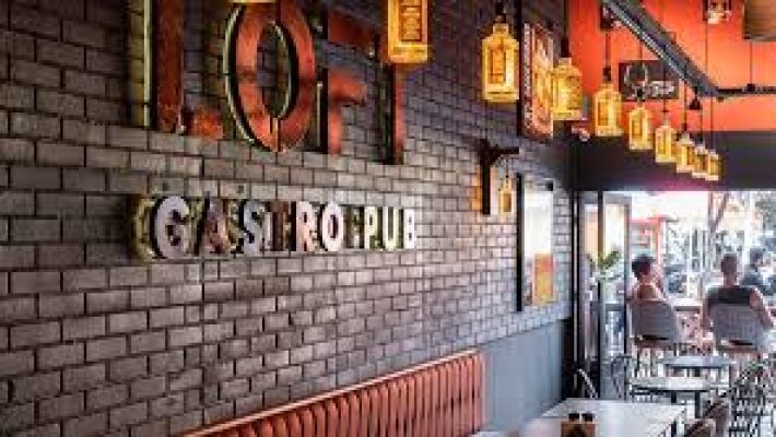 Gastro Pub’da loş ışıklar altında ahşap bir barda servis edilen özel bira çeşitleri ve gurme burger tabağı, arka planda şık ve modern dekorasyon ile birlikte görüntülenmiş