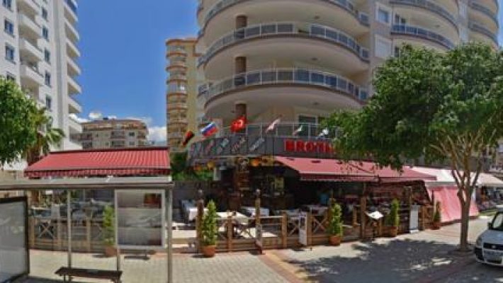 “Alanya sahilinde, palmiye ağaçları altındaki Pura Vida Restaurant’ın açık hava oturma alanı ve tropikal atmosferi.”