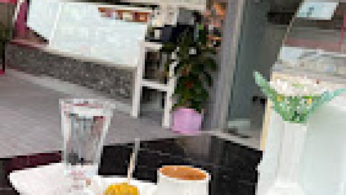 Papatyam Cafe’nin çiçeklerle süslenmiş açık oturma alanı, renkli dekorasyonu ve servis edilen kahve & tatlı tabaklarıyla birlikte gün ışığında görüntülenmiş