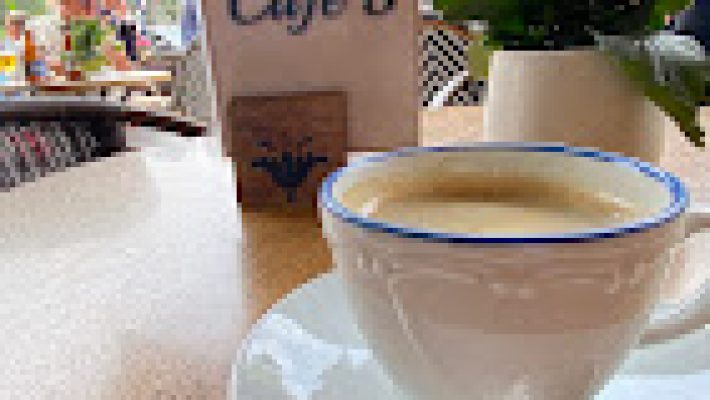 Cafe S’nin deniz manzaralı terasında renkli içecekler, kahve fincanları ve tatlı tabaklarıyla donatılmış bir masa gün batımında görüntülenmiş