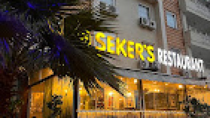 Şeker's Restaurant’ın açık hava terasında servis edilen et yemekleri, mezeler ve salatalarla donatılmış masalar; arka planda yeşillikler ve doğal ışık eşliğinde görüntülenmiş