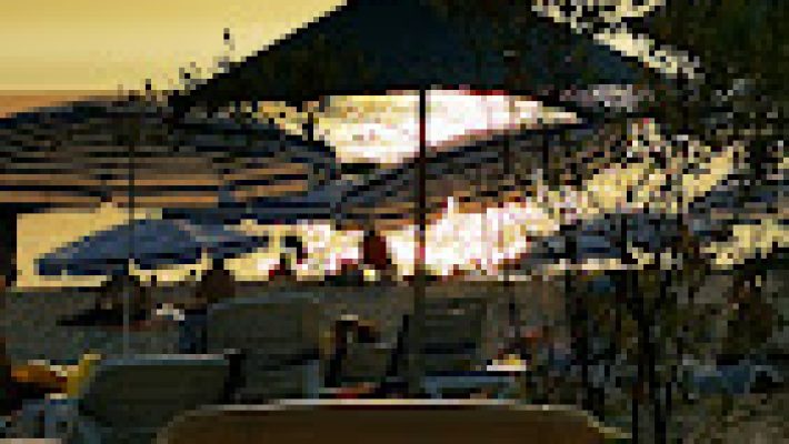 Konak Beach Park Restaurant’ın denize sıfır konumdaki masalarında servis edilen taze deniz ürünleri ve mezeler; arka planda palmiyeler ve Akdeniz manzarasıyla birlikte görüntülenmiş