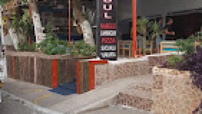 Cafe İstanbul Mek Pizza Tosmur’da servis edilen bol malzemeli, taş fırında pişmiş yuvarlak pizza; yanında ketçap, mayonez ve içecekle birlikte ahşap masada sunulmuş