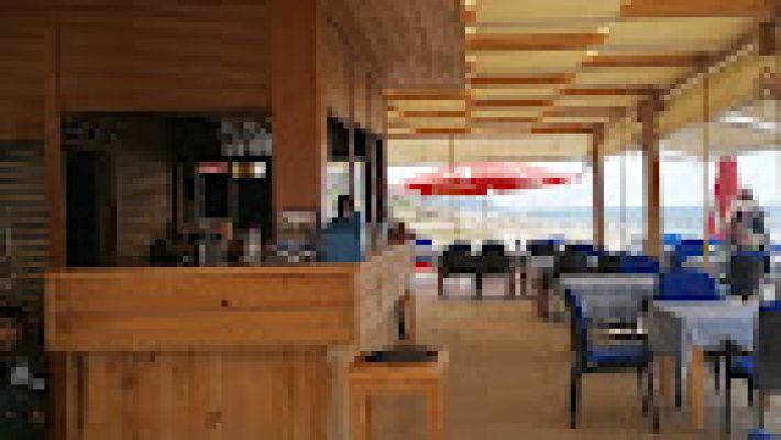 Brothers Beach Club’ın kumsalda yer alan şezlongları, tropikal kokteyllerle dolu bir masa ve arka planda Akdeniz manzarası eşliğinde gün batımı