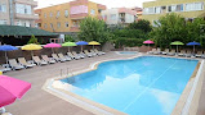 Özgür Bey Spa Hotel’in açık yüzme havuzu, modern mimarili otel binası ve palmiyelerle çevrili dinlenme alanı gün ışığında görüntülenmiş